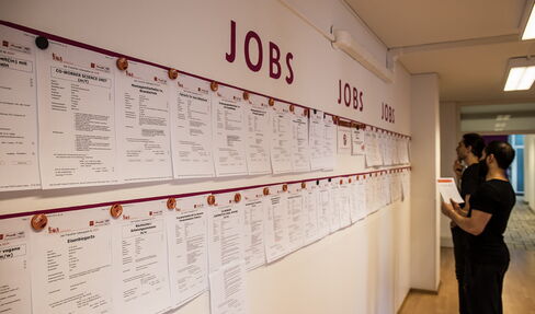 Menschen vor einer Wand, an der viele ausgeschriebene Jobs ausgehängt sind.