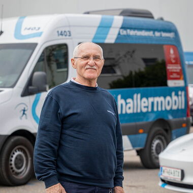 Khuseyn steht lächelnd vor seinem Dienstwagen von hallermobil und blickt in die Kamera.