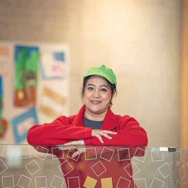 Runa steht lächelnd in Dussmann-Arbeitskleidung mit roter Jacke und hellgrüner Kappe vor der Kamera.