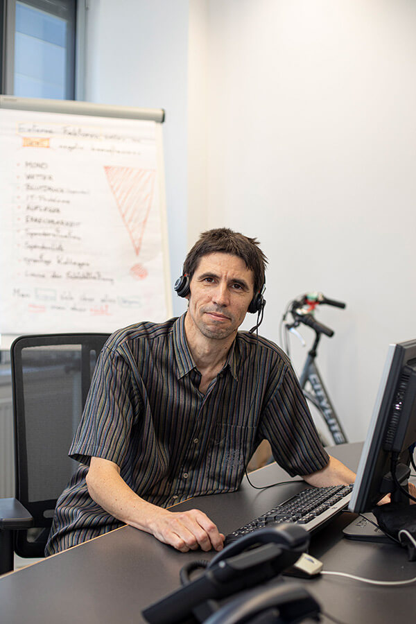 Portrait Werner Zechmann mit Headset an seinem Schreibtisch.