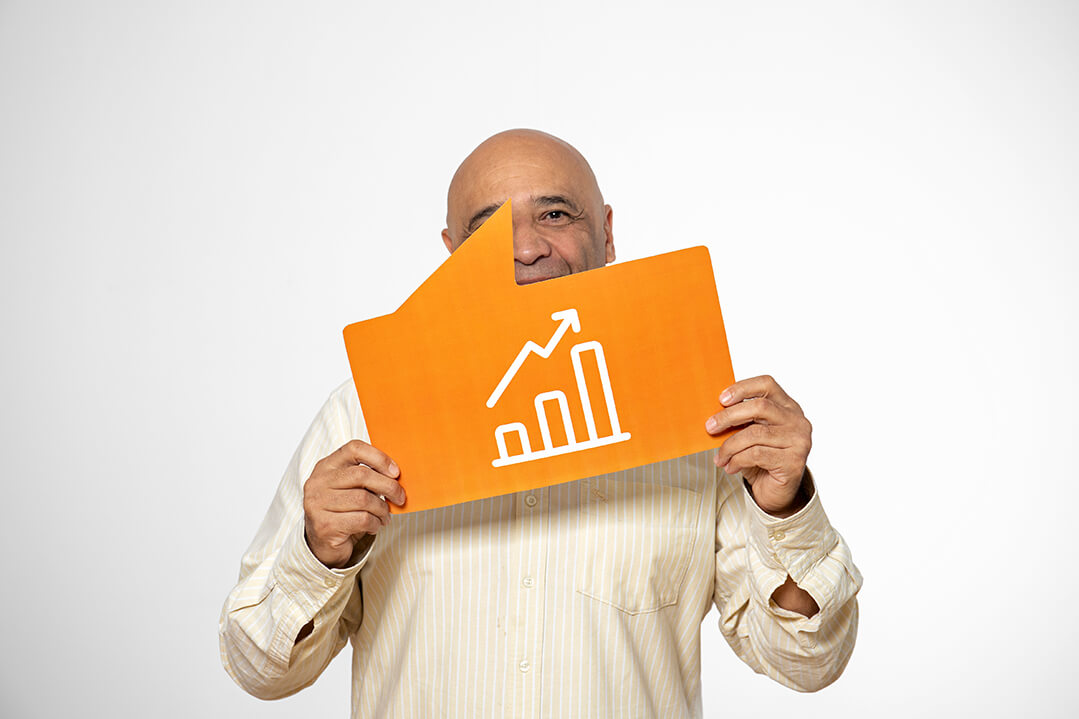 Ein lächelnder Mann über 50 in einem weißen Hemd ist in Nahaufnahme zu sehen. Sein Gesicht wird halb von einem orangen Schild verdeckt, das die Form einer Sprechblase hat und auf dem ein Balkendiagramm und ein nach oben zeigender Pfeil abgebildet sind.
