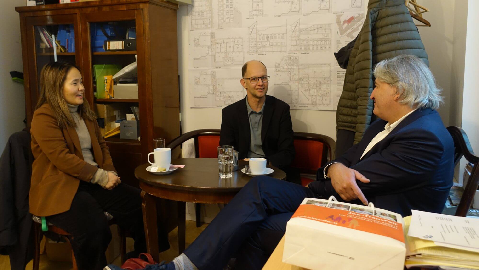 Thomas Rihl, Zita Oyuntuul Chuluun und Gerald Schmid im Gespräch an einem Tisch im Büro von Gerald Schmid.