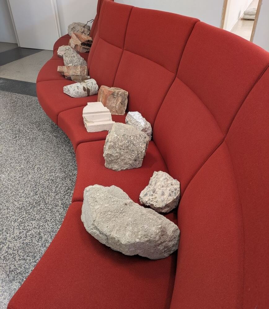 Zehn Steine gleichmäßig nebeneinander auf einer Couch arrangiert, Teil einer aktuellen Kunstausstellung.
